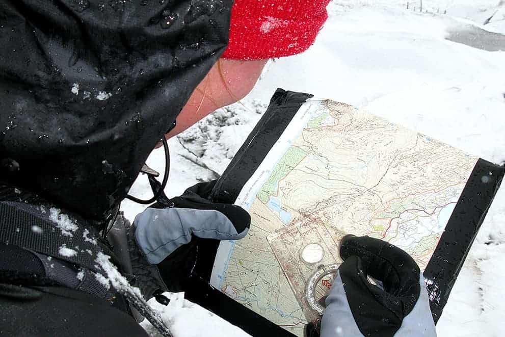 A lady with a map and compass practicing map reading in winter on a hill in the Peak District