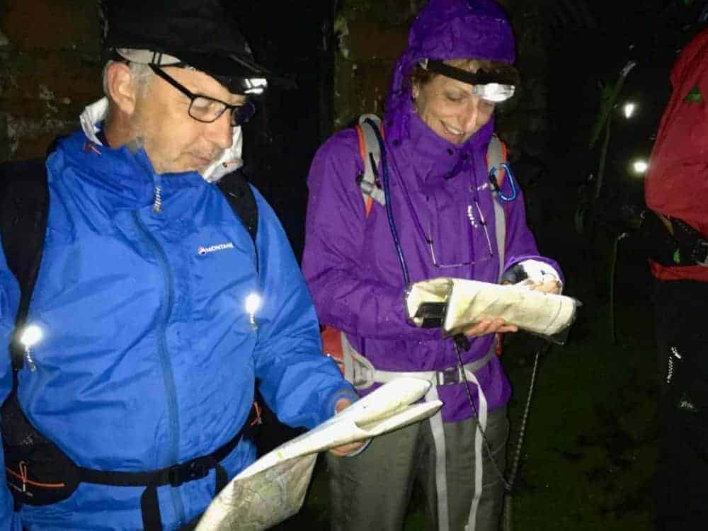 A man and a lady study their maps by torchlight on a night navigation course in the Peak District.