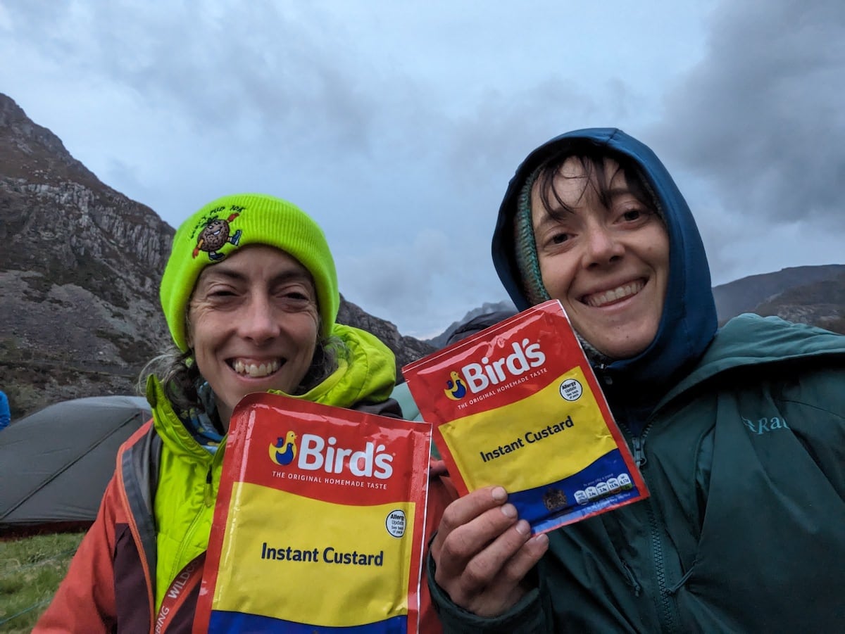 Two women holding sachets of Birds Instant Custard up to the camera in a selfie