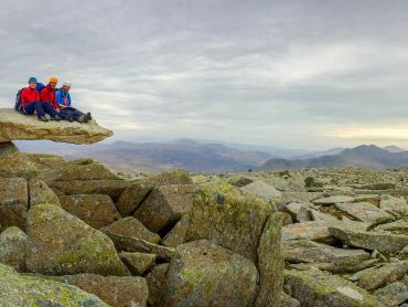 Three people sit on the cantilever stone in Snowdonia after scrambling on a mountaineering skills course