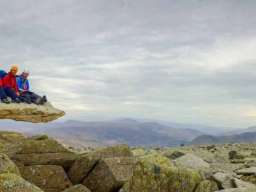 A group of mountaineers sits on the Cantilever stone on Glyder Fach, in Eryri (Snowdonia)