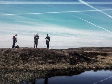 Three people stand by a small moorland pond whilst practicing navigation on a Hill and Moorland Leader Award training course