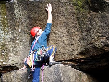A young man stretches for a hold whilst on a Peak District rock climbing instructor course.