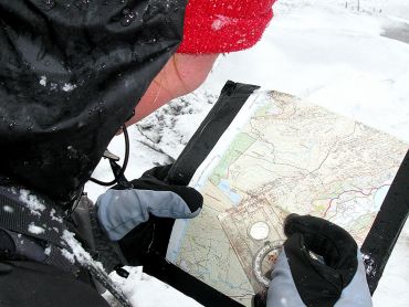 A lady with a map and compass practicing map reading in winter on a hill in the Peak District 