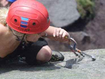 A lady rock climbing and placing gear whilst on a Rock Climbing Instructor (RCI) course in the Peak District national park