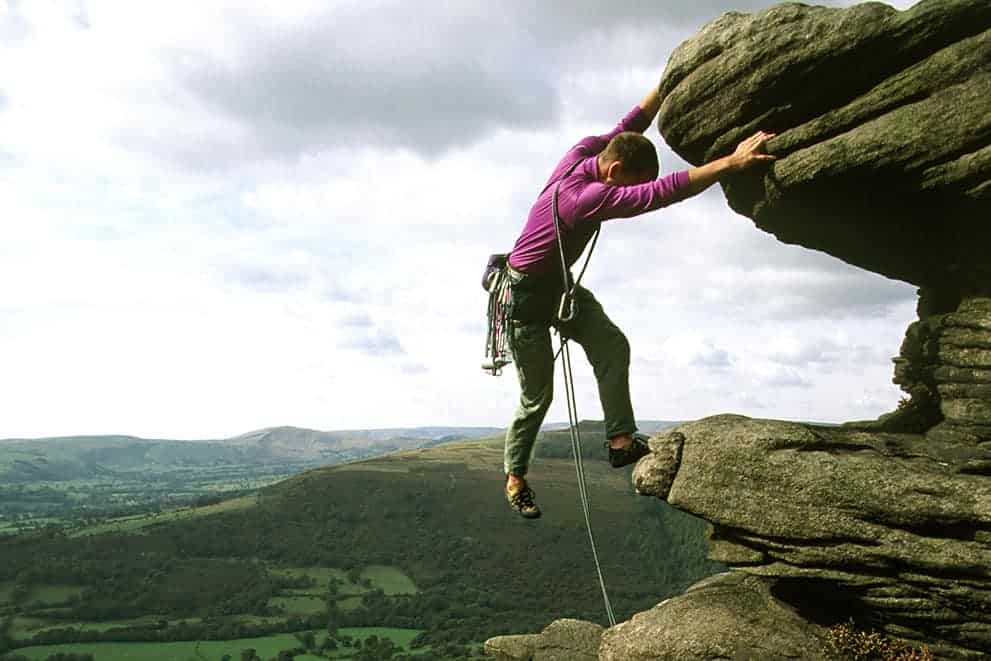 A young man stretches for a hold whilst on a Peak District rock climbing instructor course.