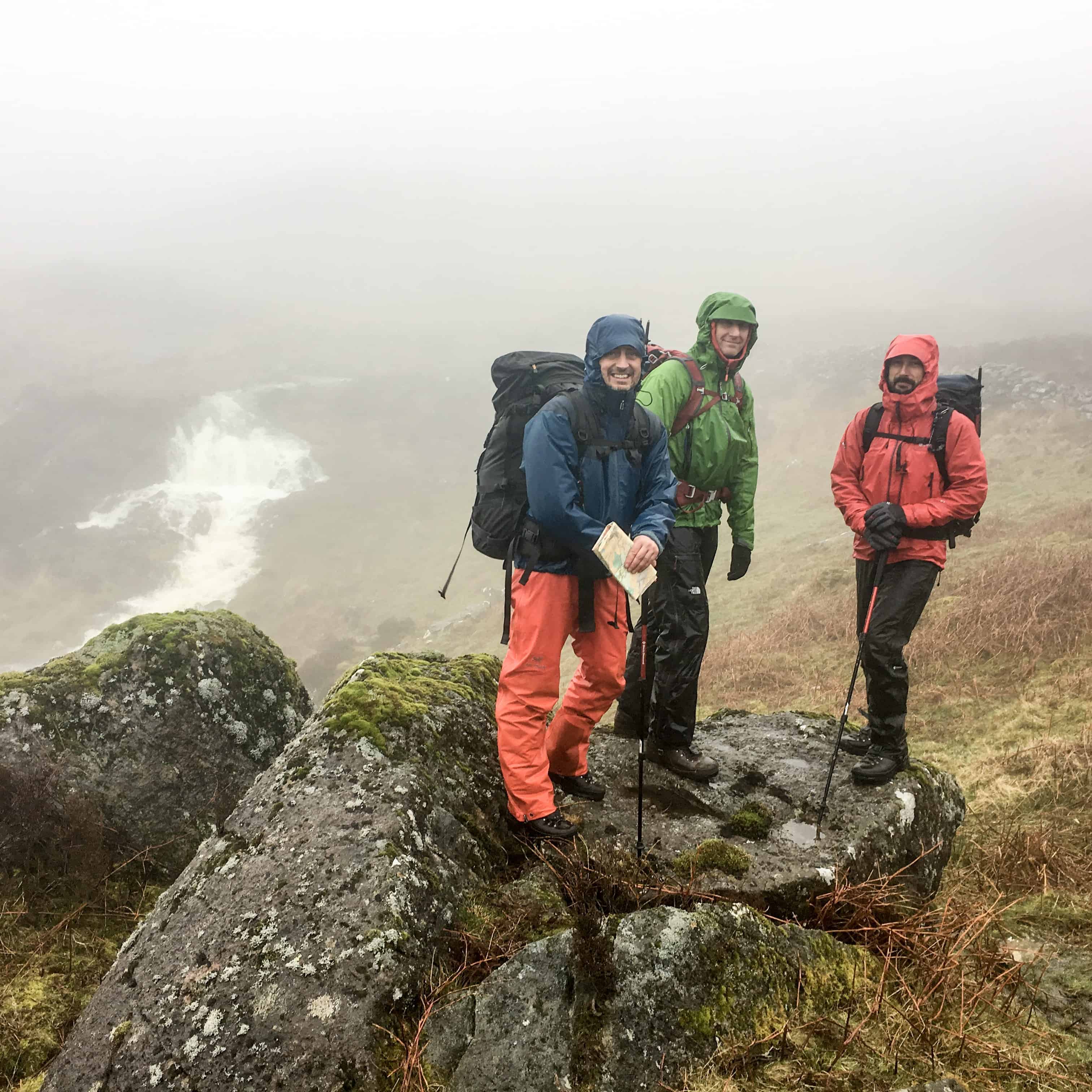 A group of three men in pouring rain on a Mountain leader assessment in Wales.