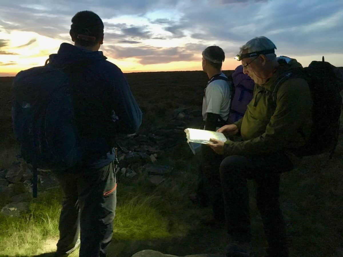 Night navigation course in the Peak District. 3 men with head torches, map and compass.