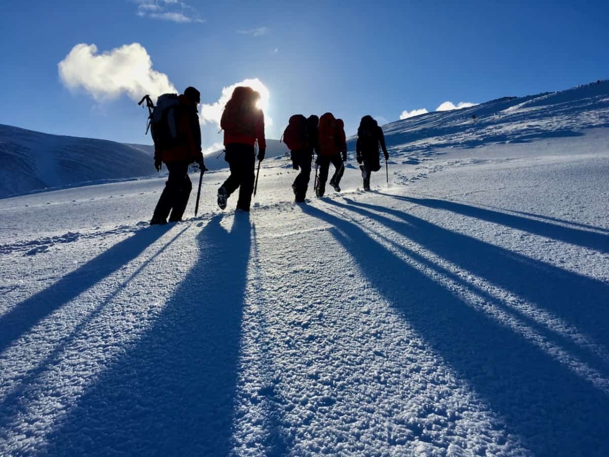 Winter walkers with ice axes and crampons heading up a hill in Scotland on a winter skills course.
