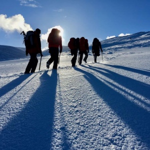 Winter walkers with ice axes and crampons heading up a hill in Scotland on a winter skills course.
