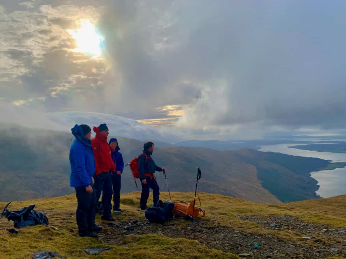 Four people on a mountain top looking down a Loch on a guided walking holiday in Scotland.