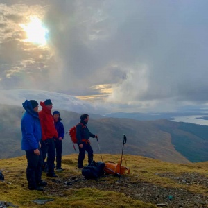 Four people on a mountain top looking down a Loch on a guided walking holiday in Scotland.