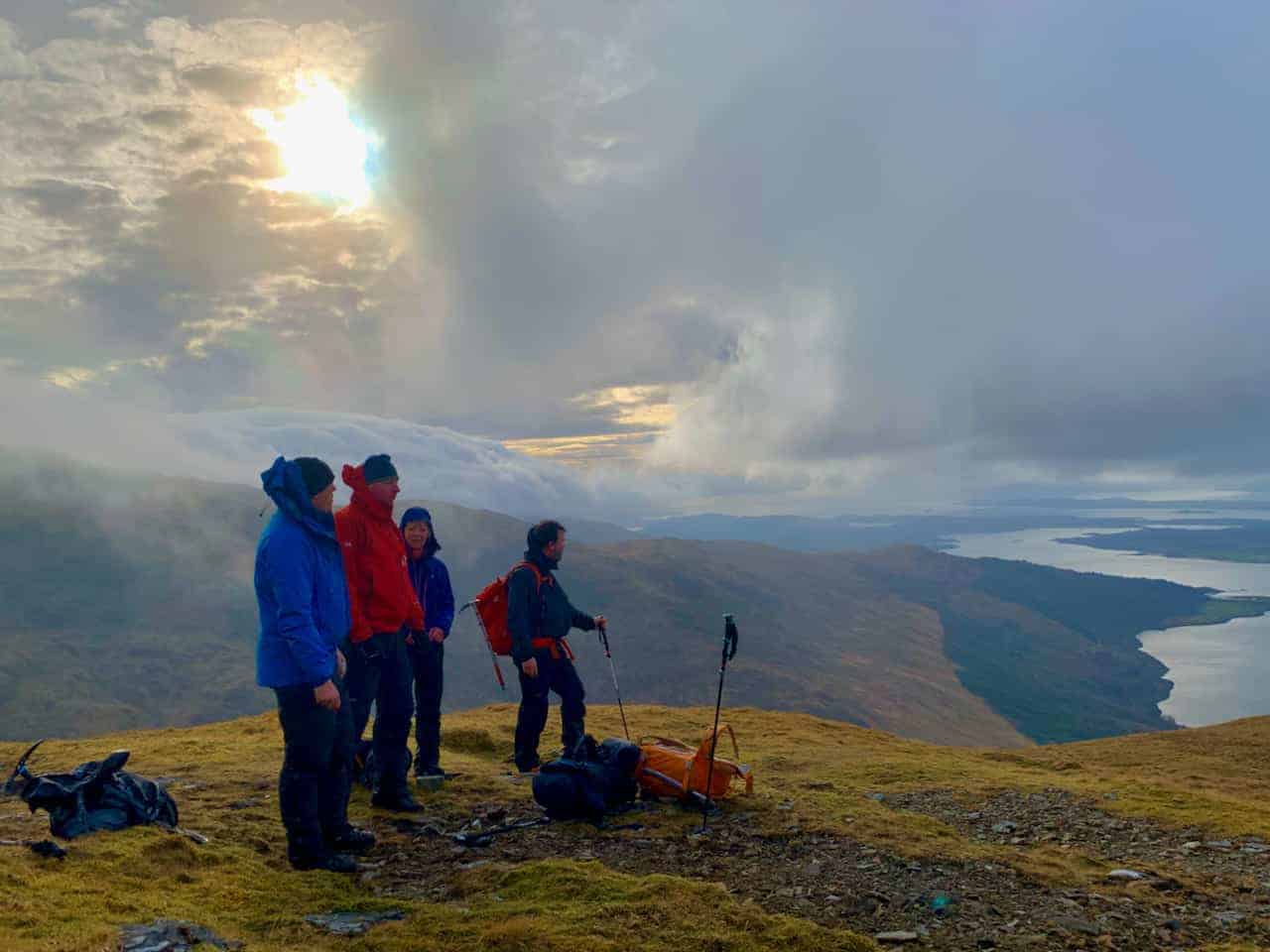 Four people on a mountain top looking down a Loch on a guided walking holiday in Scotland.