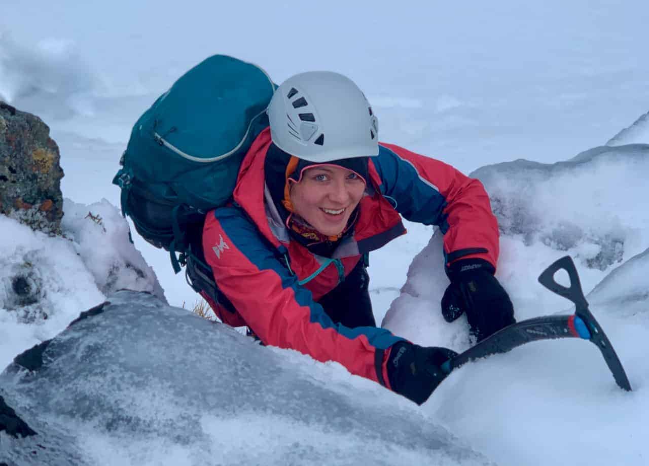 A lady winter walking with ice axe and crampons on a winter skills course in Scotland