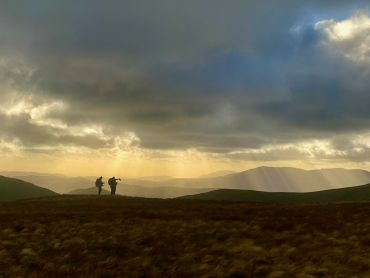 3 people look at a map whilst standing on a summit in Snowdonia on their Mountain Leader course.