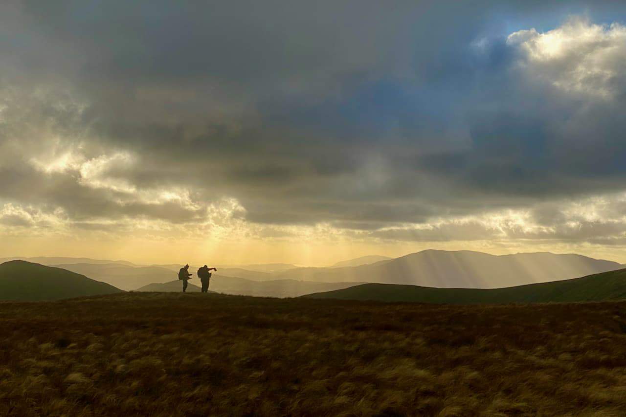 3 people look at a map whilst standing on a summit in Snowdonia on their Mountain Leader course.
