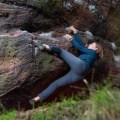 woman bouldering on a rock wearing blue bouldering pants and green top