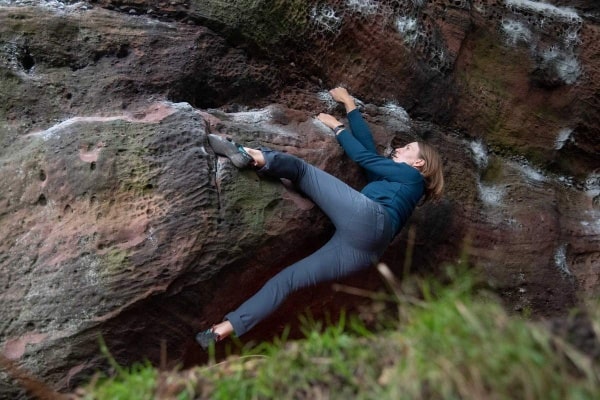 woman bouldering on a rock wearing blue bouldering pants and green top
