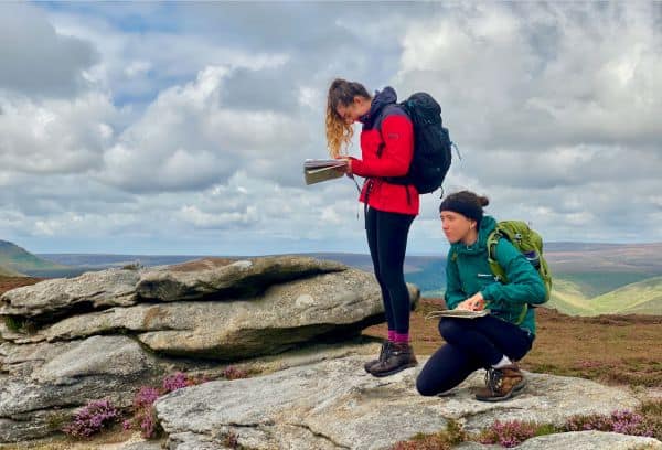 Two ladies use a map and compass whilst navigating on Kinder Scout on a navigation course.