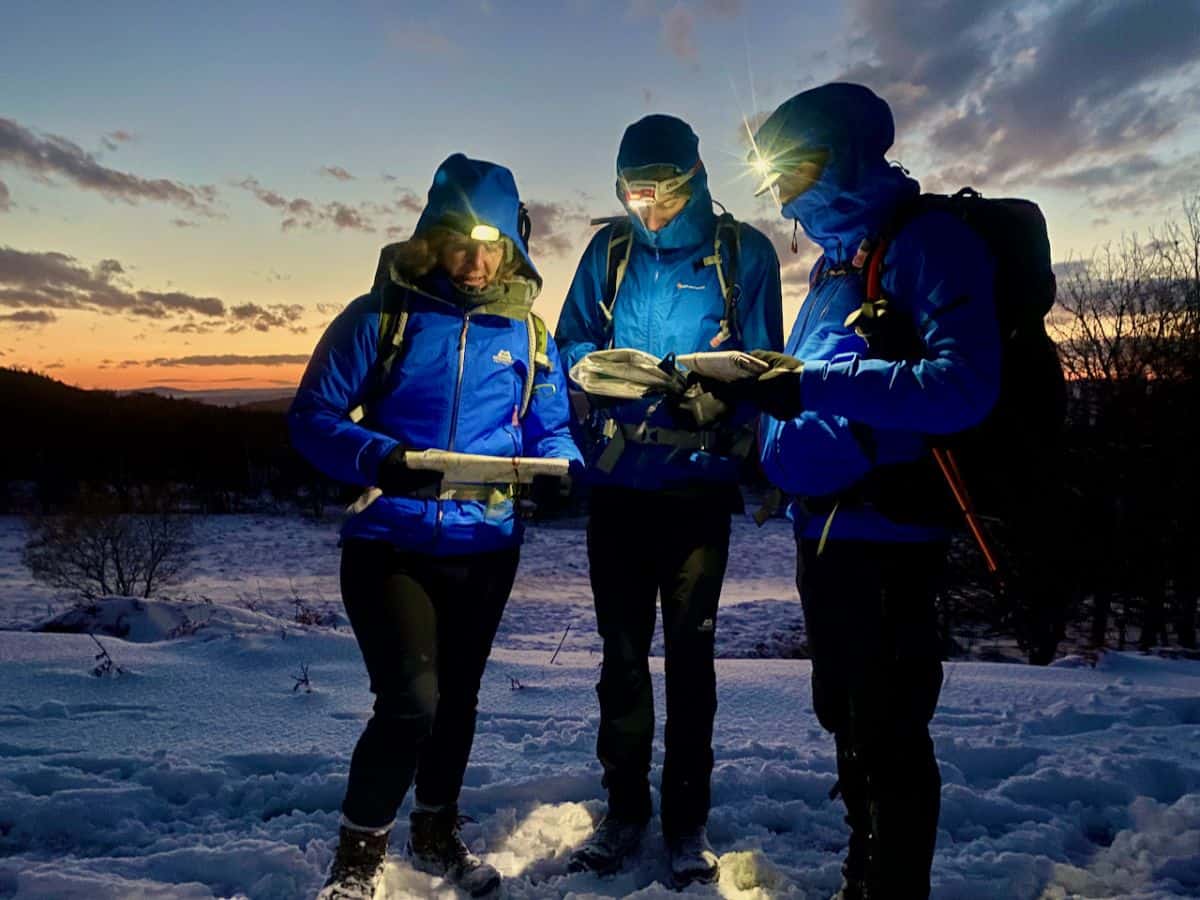 Three people using head torches to map read at night on a night navigation course in The Peak District