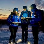 Three people using head torches to map read at night on a night navigation course in The Peak District