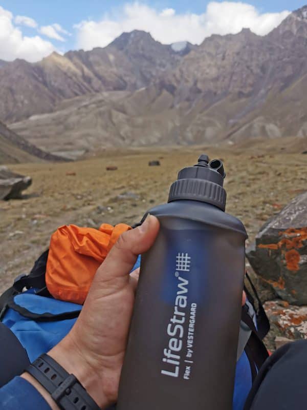 A hand holding a collaspible water filter bottle with mountains in the background
