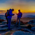 A group learn navigation using a map and compass as the sun sets whilst on a navigation course in the peak District.