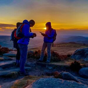 A group learn intermediate navigation using a map and compass as the sun sets whilst on a navigation course in the peak District.