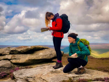 Two women in the Peak District looking at their map and compass whilst on an introduction to navigation course.