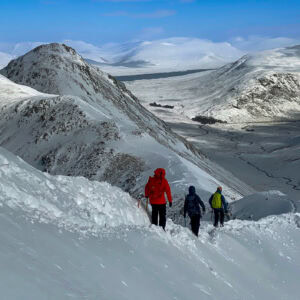 A group of winter mountaineers, descends down a snowy ridge in Scotland on Buaichille Etive Beag.