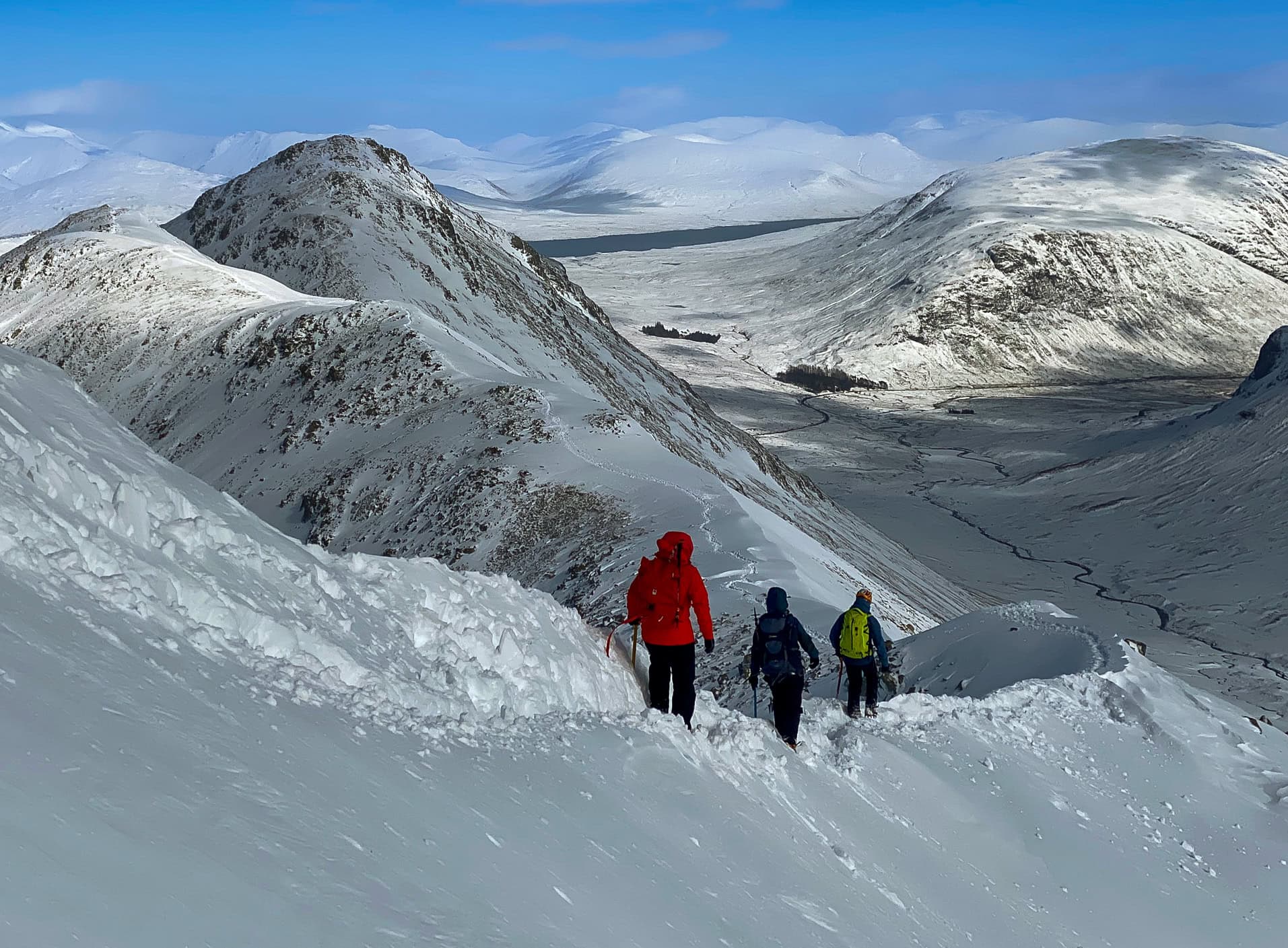A group of winter mountaineers, descends down a snowy ridge in Scotland on Buaichille Etive Beag.