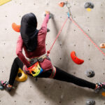 A female muslim climber leads a climb on an indoor wall for her Climbing Wall Development Instructor.