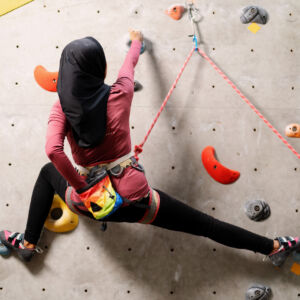 A female muslim climber leads a climb on an indoor wall for her Climbing Wall Development Instructor.