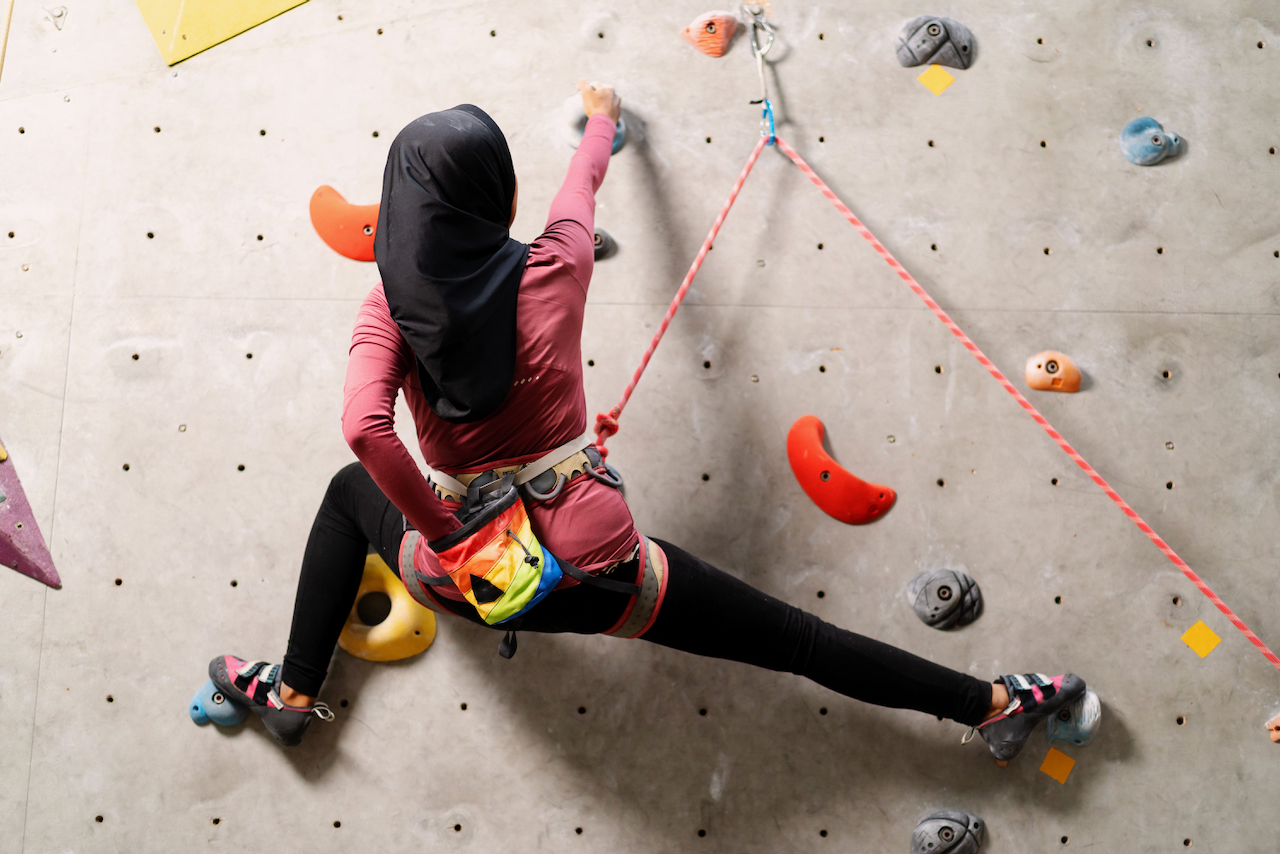 A female muslim climber leads a climb on an indoor wall for her Climbing Wall Development Instructor.