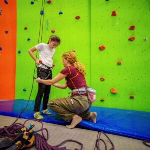 A climbing instructor helping a child with a climbing harness at a climbing wall.