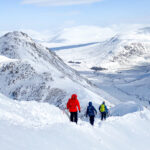 Three people descend a snow covered ridge on a Introduction to Scottish Winter Mountaineering / Skills course.
