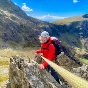 A woman scrambling up rocks on Cneifon arete in Eryri (Snowdonia) on a scrambling course.