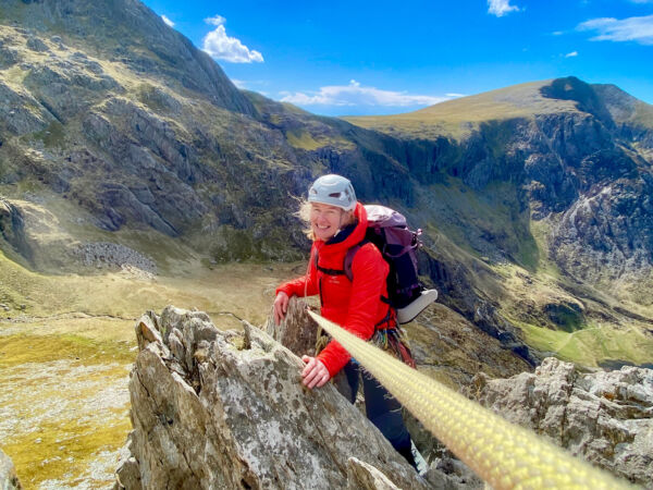 A woman scrambling up rocks on Cneifon arete in Eryri (Snowdonia) on a scrambling course.