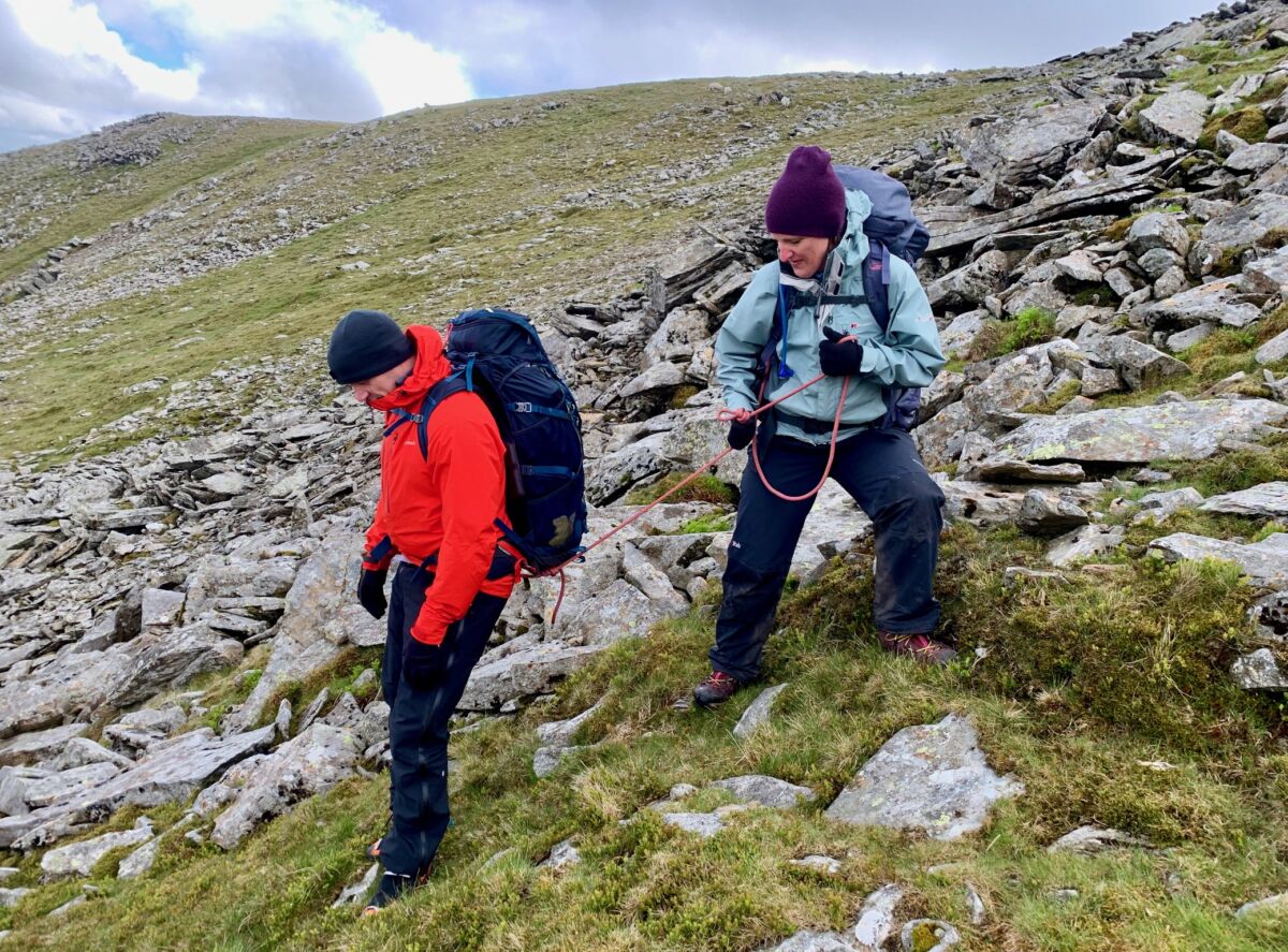 A woman confidence roping a man on a Mountain leader training course in Wales.