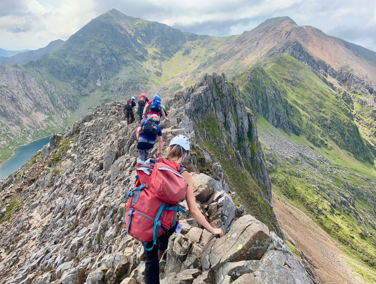 A group on a Mountain Leader training course walk along Crib Coch. Snowdon summit is in the background.
