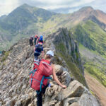 A group on a Mountain Leader training course walk along Crib Coch. Snowdon summit is in the background.