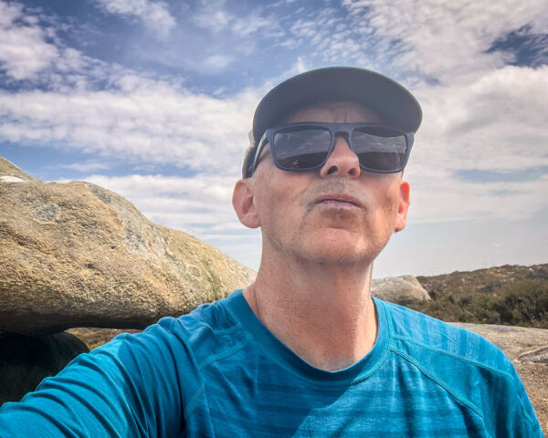 A man wearing Sungod Renegades sunglasses in rocky environment with blue skies