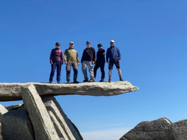 A group stands on the Cantilever stone on Glyder Fach on a Mountain Leader course.