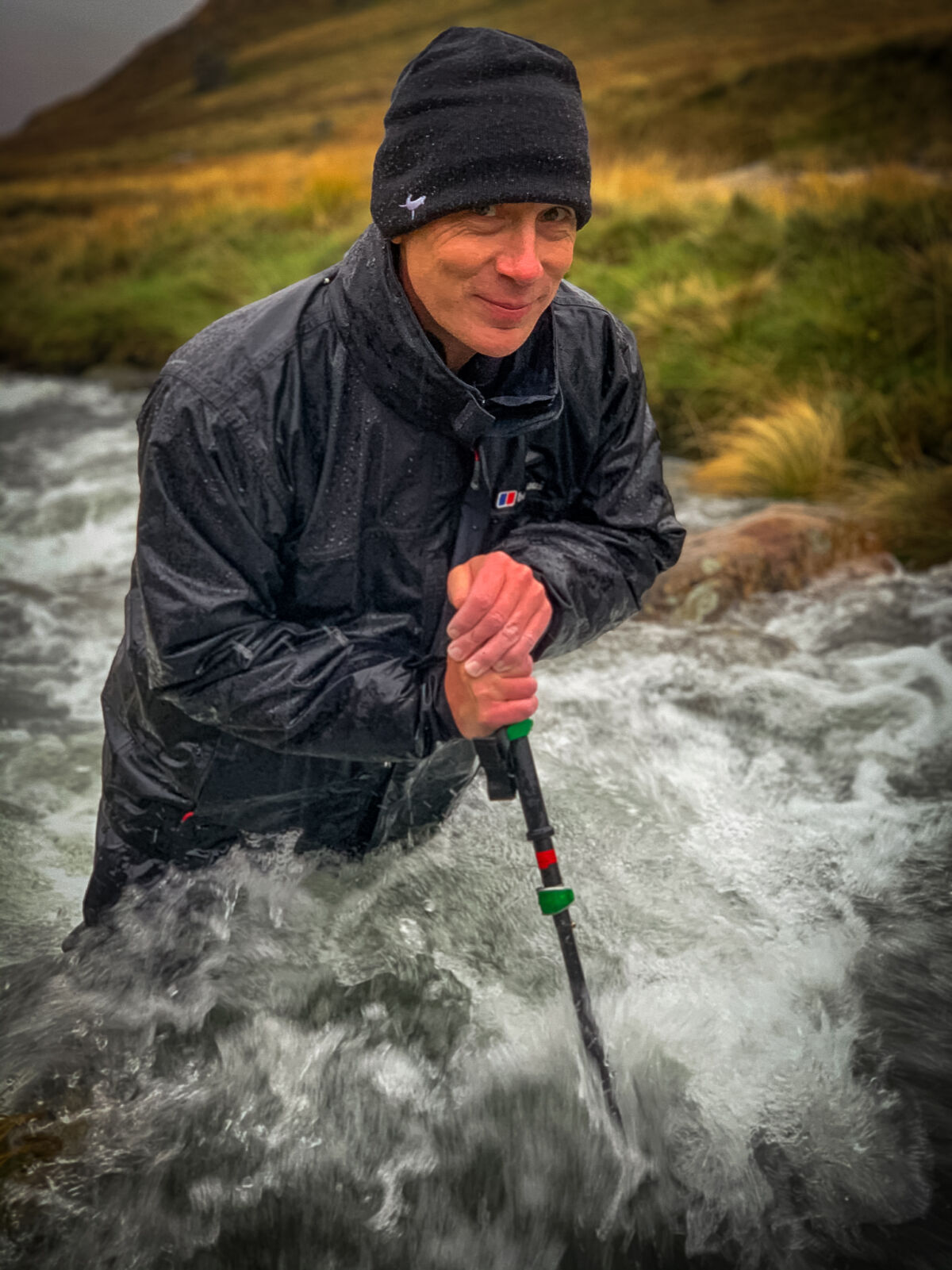 A man wades across a mountain stream with a pole on a Mountain Leader course.