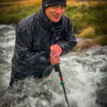 A man wades across a mountain stream with a pole on a Mountain Leader course.