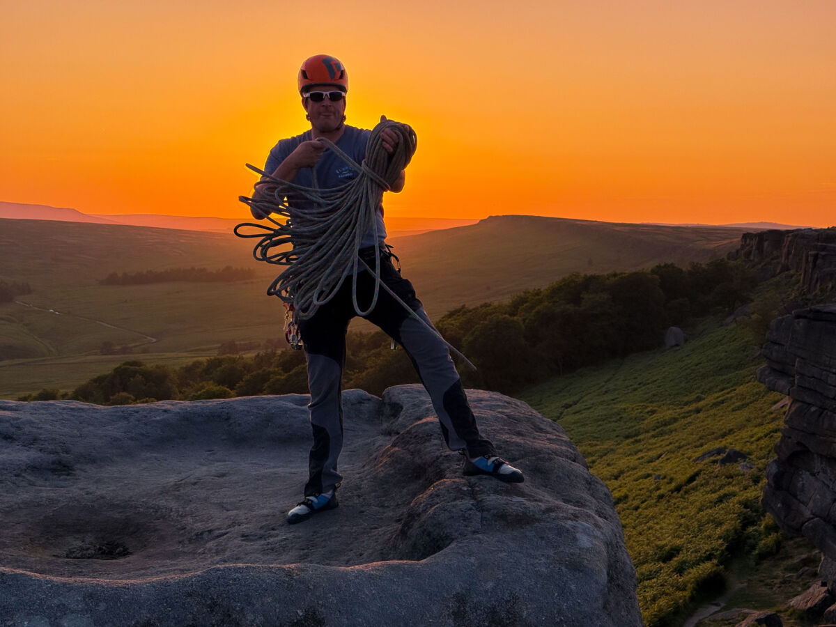 A man coiling a rope at sunset after lead climbing in the Peak District.