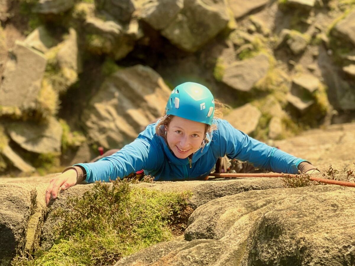 A lady climbing a rock face with a rope on a rock climbing course in the Peak District.