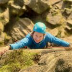 A lady climbing a rock face with a rope on a rock climbing course in the Peak District.