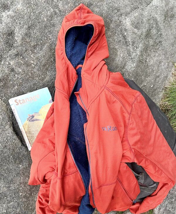 A red Rab Evolute Hoody climbing and walking jacket on gritstone rock next to a Stanage Edge rock climbing guidebook