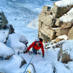 A man smiling as he climbs the crux of a winter route on a winter mountaineering course in Aviemore, Scotland.